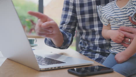 close up of working father using laptop at home on kitchen counter whilst looking after young daughter - shot in slow motion