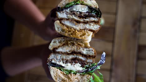 close up in 4k of a chicken cutlet sandwich with lettuce and burrata on french brea, that's just been cut in half and opened to reveal the filling by hands with a perfect manicure