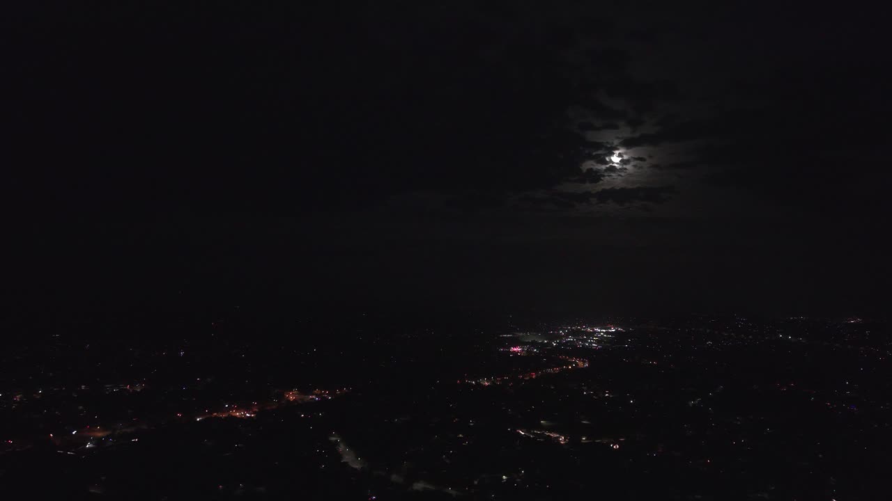 Un affascinante video realizzato con drone cattura una città australiana di notte, illuminata dalla luce lunare. La scena mostra le luci della città, i cieli coperti di nuvole e una tranquilla atmosfera dall'alto