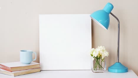 pila de libros, tablero en blanco, jarrón de flores, taza de té y lámpara de mesa
