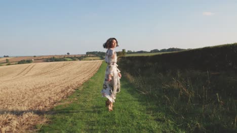 young woman in a long dress walks through a field and spins