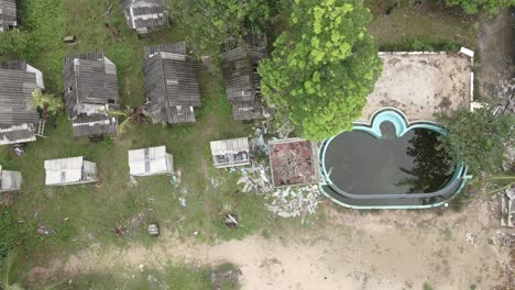 aerial birds eye view left moving trucking shot of a abandoned derelict destroyed beach resort with dirty swimming pool on the island of koh chang ,from the effects of covid 19