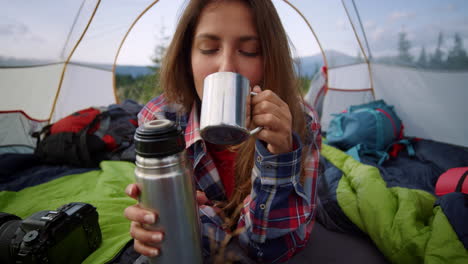 Woman-drinking-hot-tea-from-thermos-in-the-tent