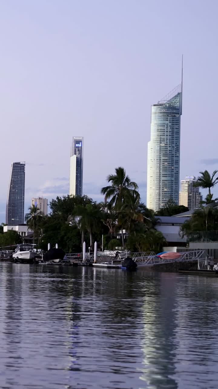 Una composizione verticale che mostra alti edifici moderni che si riflettono nell'acqua calma di un fiume durante il crepuscolo.