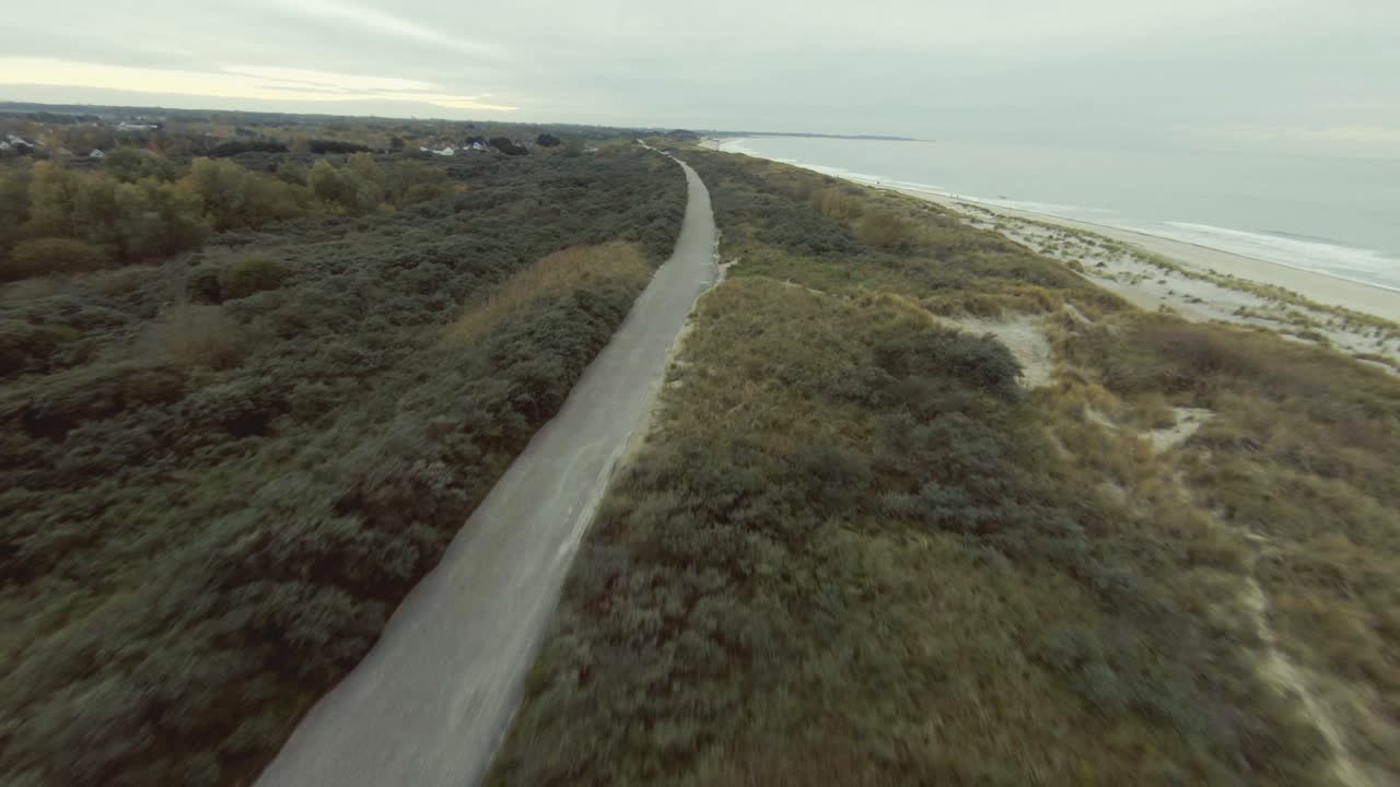 drone volando bajo sobre las dunas en una playa holandesa siguiendo una carretera en la parte superior del dique