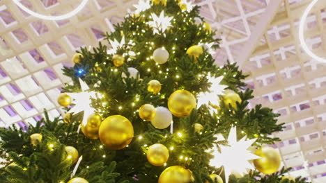 large christmas tree with gold and white ornaments in a modern building