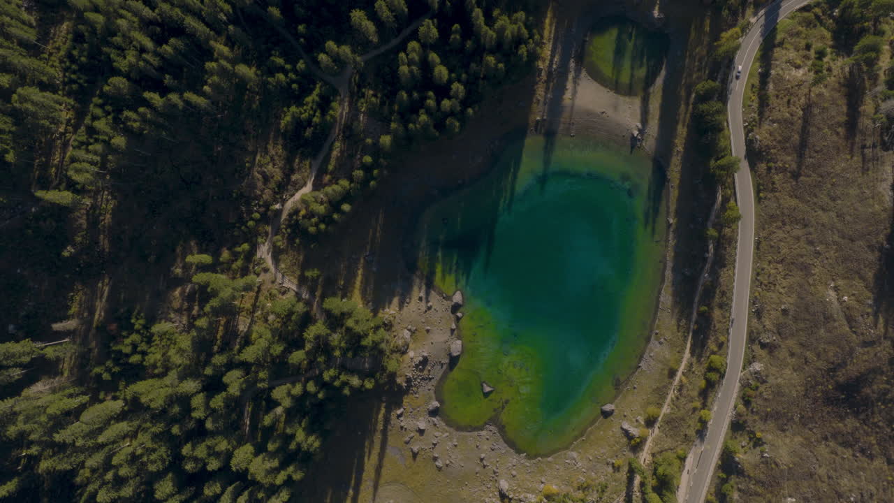 Cinematic aerial view of emerald alpine lake surrounded by forest, rocky shoreline and mountain landscape in the Dolomites, Italy tranquil nature scenery from drone