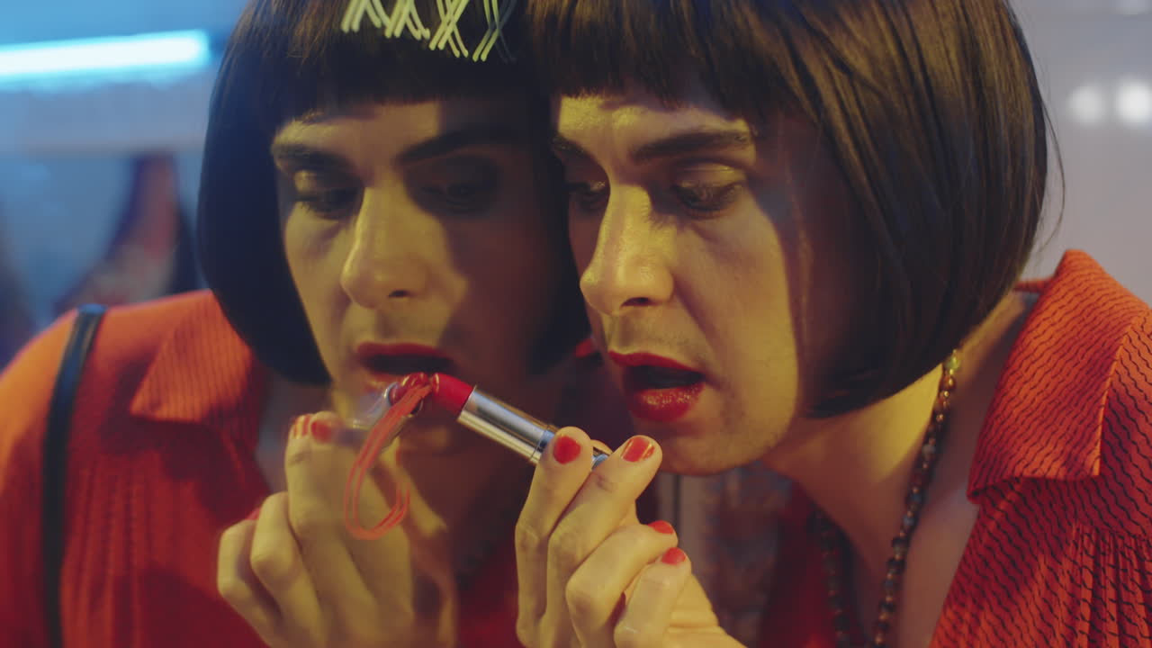 hombre transgénero dibujando con lápiz labial en el espejo en el baño de un club nocturno