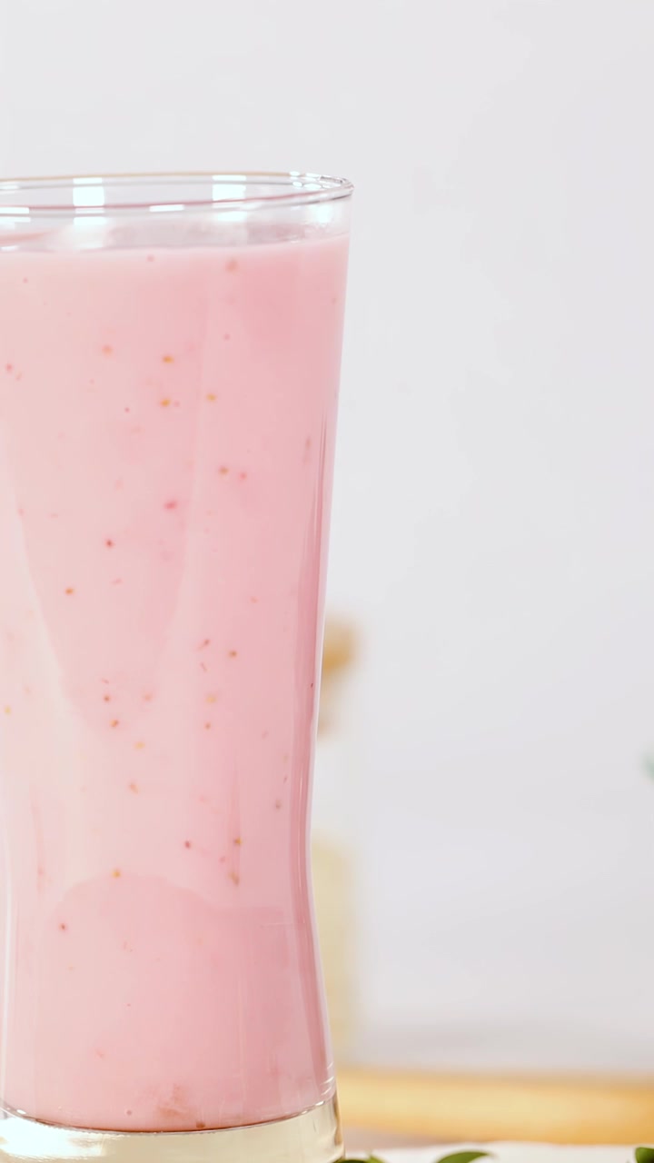 Frullato cremoso rosa alla fragola in un bicchiere, illuminazione brillante, lenta carrellata in avanti della telecamera, rinfresco estivo.