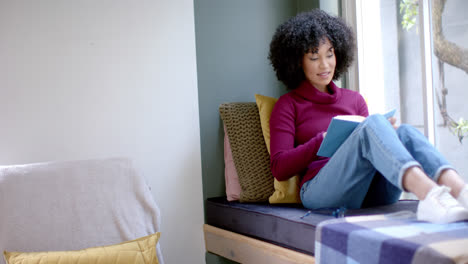 mujer biracial feliz leyendo un libro en casa, cámara lenta, espacio de copia
