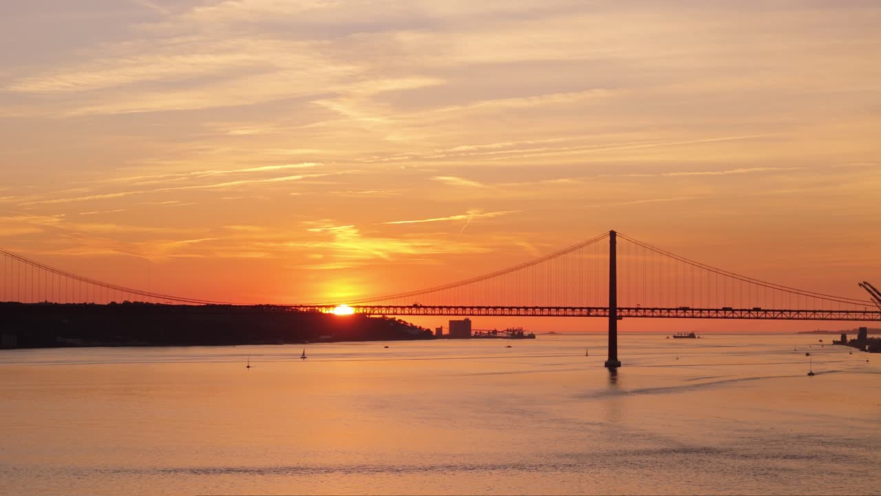 Panoramischer Luftschwenk, während die Sonne hinter einem entfernten Hügel über dem Tejo untergeht, vorbei an der Hängebrücke in Lissabon, Portugal