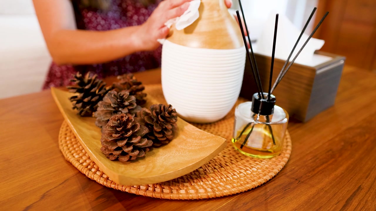 Femme nettoyant un vase décoratif et des pommes de pin sur une table en bois
