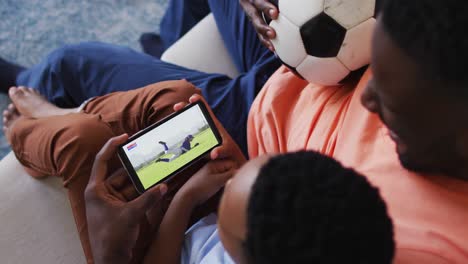 Compuesto-De-Padre-E-Hijo-En-Casa-Viendo-Un-Partido-De-Béisbol-En-Un-Teléfono-Inteligente