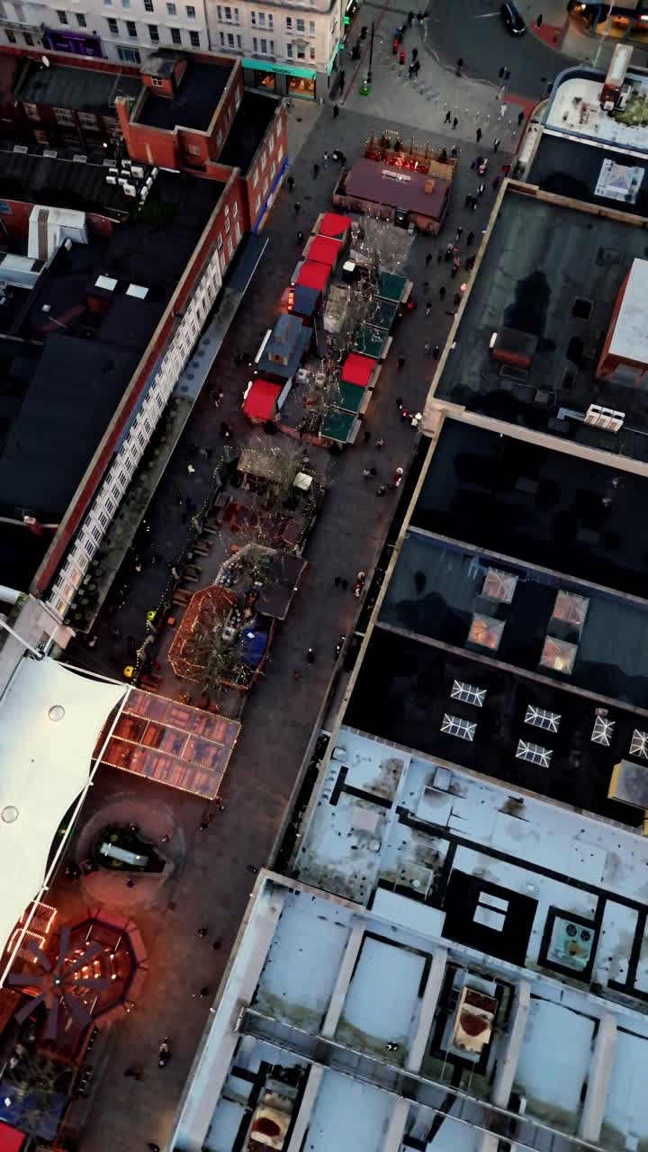 Bird’s-eye aerial drone shot panning over Southampton’s winter Christmas Market at sunset, showcasing glowing festive stalls, crowds moving through the square, and the city bathed in warm light