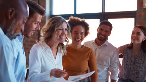 businesswoman leading team meeting in busy multi-cultural office handing out documents