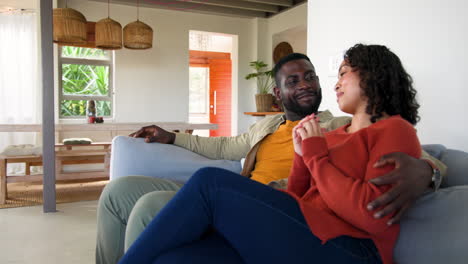 multiracial couple relaxing on couch at home, sharing joyful moment