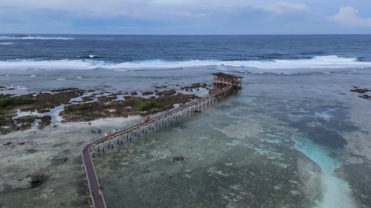 Drone view of Cloud 9 Surfing Area in Siargao, Philippines, showing turquoise ocean, shallow reef, wooden pier, and famous surf observation deck surrounded by clear tropical water and gentle waves