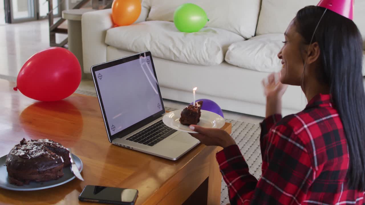 mujer de raza mixta usando una computadora portátil teniendo un video chat de cumpleaños sosteniendo un pastel