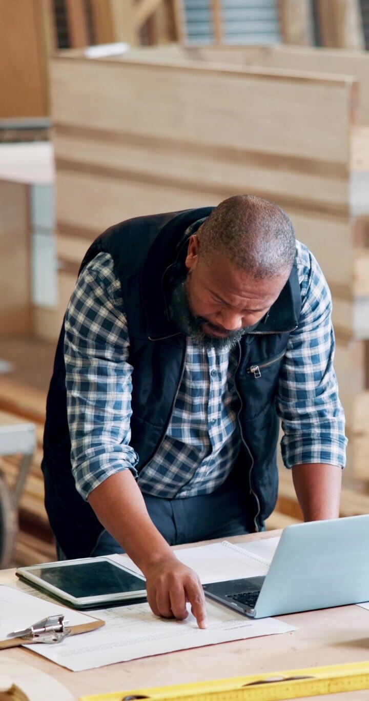 Carpenter Working on Laptop and Blueprints in Workshop