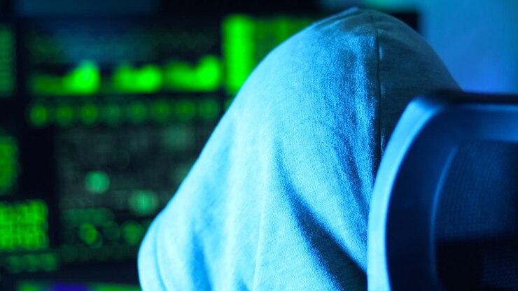Russian hacker in white hoodie in front of a computer screen showing green matrix-style data