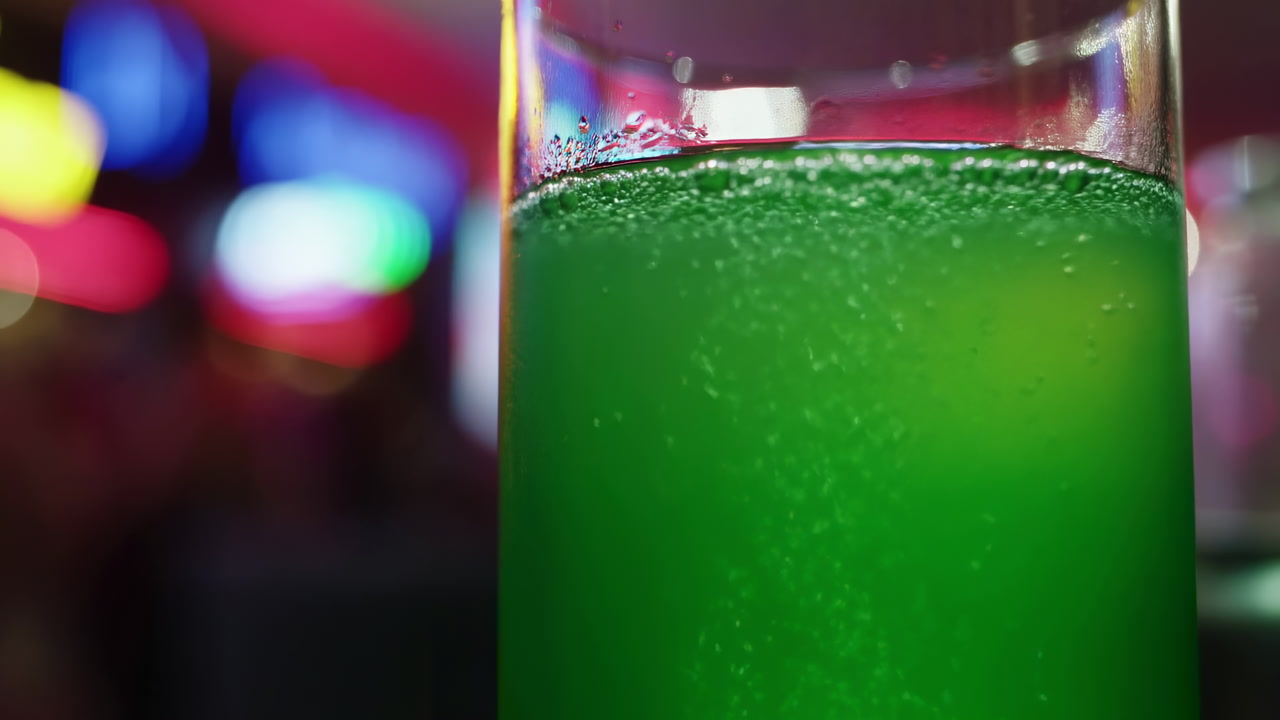 Green Fizzy Drink In Glass, Closeup Of Effervescent Cocktail With Condensation On Rim, Bubbles Rising