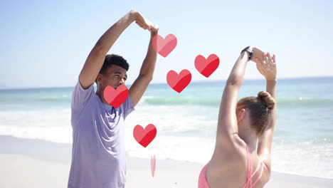 animation of red hearts over diverse couple stretching on beach