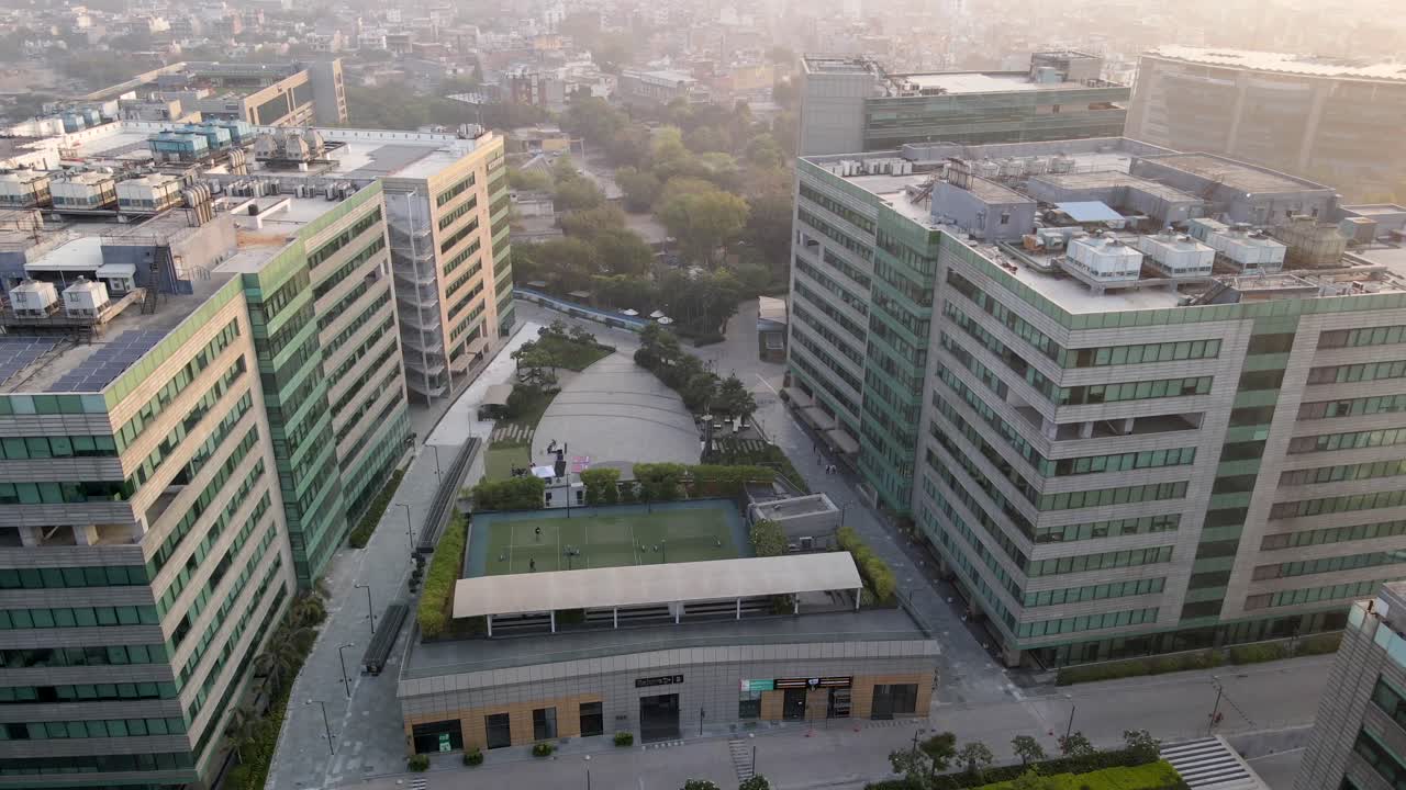 Sweeping drone shots of a sleek business park in Gurgaon, Haryana—glass skyscrapers, landscaped greenery, and urban infrastructure reflecting India’s growing global corporate presence