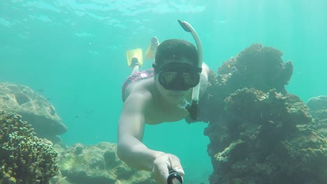 hombre buceando y nadando bajo el agua entre corales y peces selfies