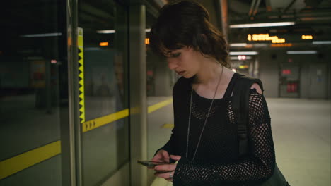 mujer esperando y usando el teléfono móvil en la plataforma de la estación de tren subterráneo de londres en tiempo real 1