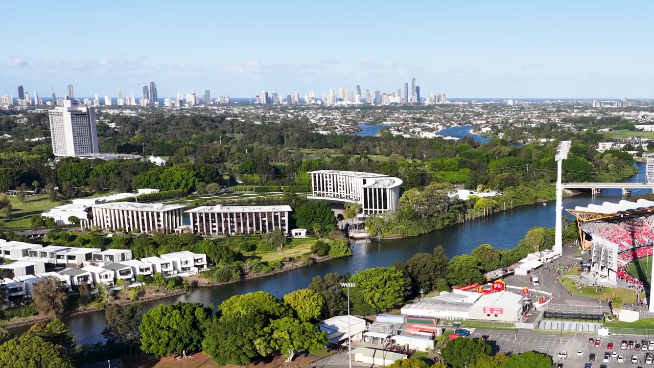 Ampia ripresa aerea con drone di una moderna arena sportiva e un fiume con lo skyline della città in lontananza.