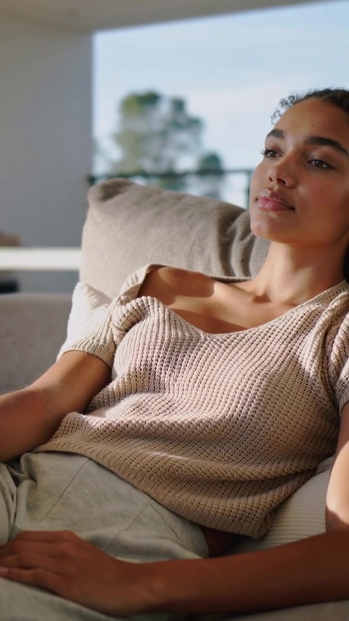 Vertikal video: Kamera panorerer tilbage og viser kvinde på sofa, lukker øjnene, trækker vejret, hviler derhjemme i beige strik