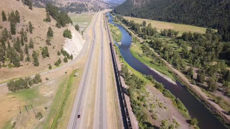 Arial-shot-of-train-driving-along-highway-and-river-on-USA's-westcoast