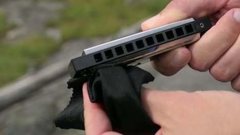 man wiping harmonica with micro fiber cloth in nature outdoors, close up