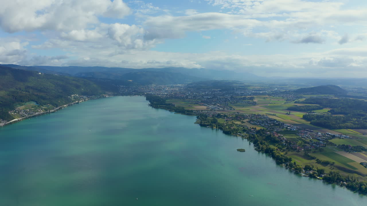 Aerial view of 'Lake Biel' in Switzerland in with clear greenish-blue water surrounded by a scenic landscape on a sunny day. City of Biel in the background under blue sky with fluffy clouds