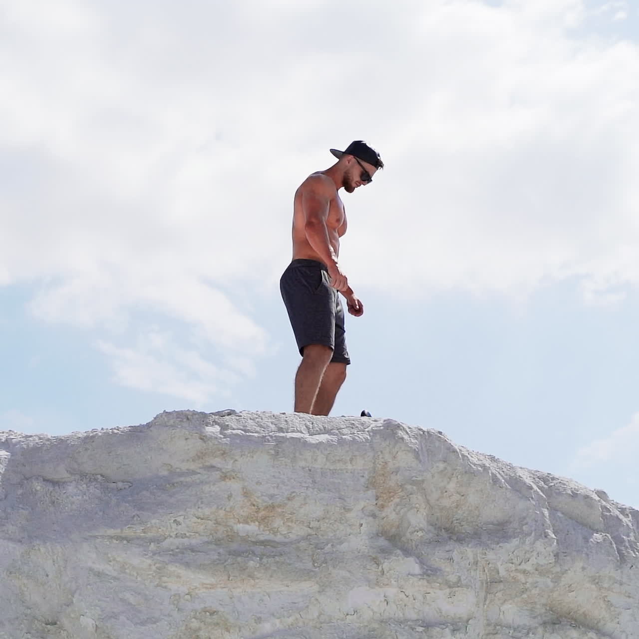 Atleta sem camisa com boné e óculos na montanha. Vista de baixo de um esportista no topo de uma colina branca.