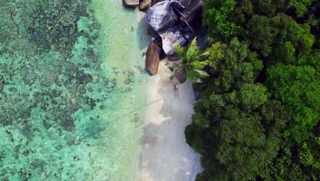 Agua-Turquesa-Que-Baña-Suavemente-Una-Playa-De-Arena-Rodeada-De-Rocas-De-Granito-Y-Exuberante-Vegetación-Tropical.