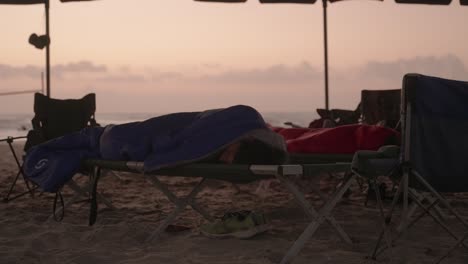 Obdachloser-Junge-Schläft-Bei-Sonnenaufgang-Auf-Einem-Kinderbett-Im-Blauen-Schlafsack-Am-Strand