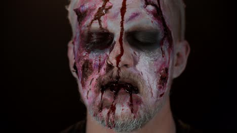 Close-up-of-sinister-man-with-horrible-scary-Halloween-zombie-make-up-blood-flows-and-drips-on-face