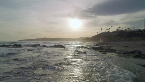 Aerial-moving-forward-near-the-rocks-at-the-beach,-with-sun-reflecting-on-the-water