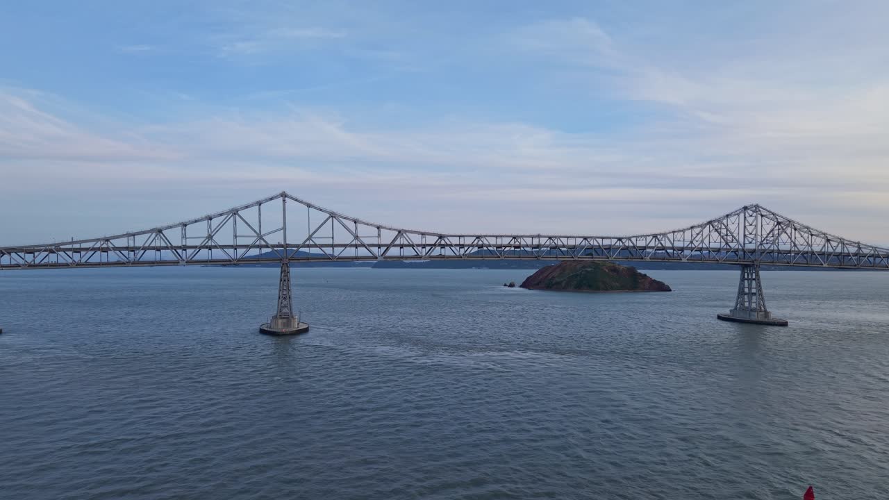 Sweeping drone view of the bridge captures a long expanse of steel above glinting water and softly rolling clouds on the horizon.