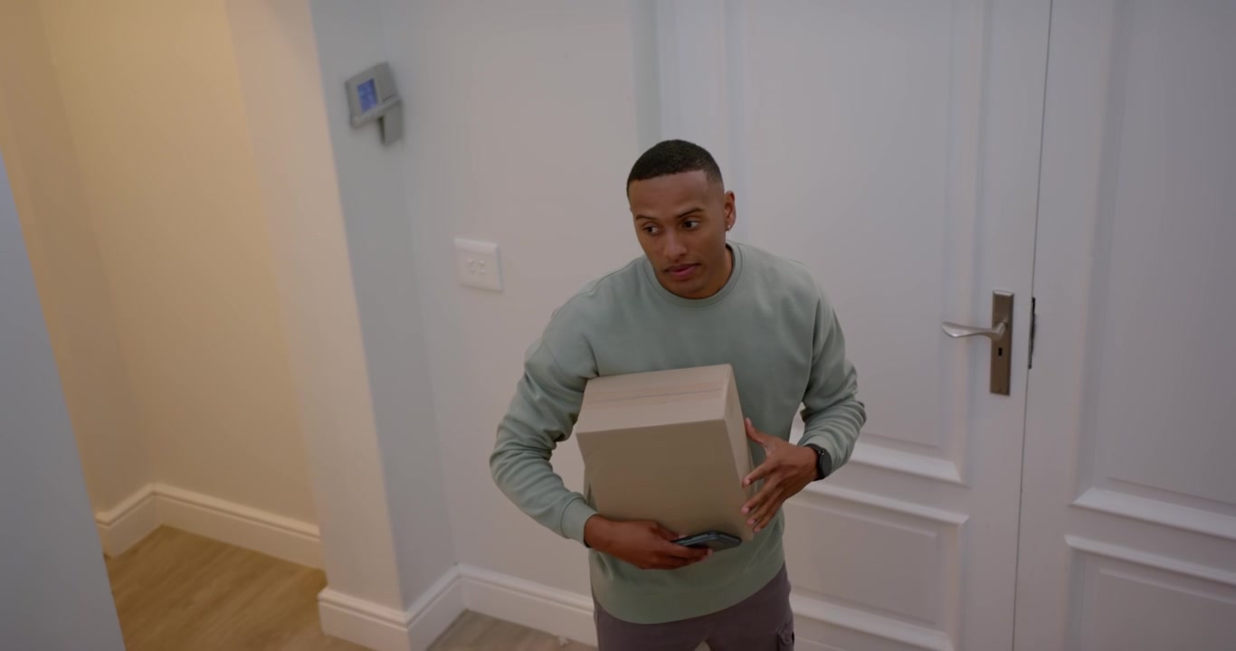 African American man carrying package entering foyer, locking door checking phone after delivery