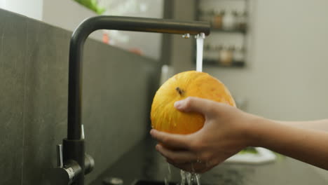 a woman washes a ripe melon under the kitchen faucet