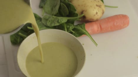 Pouring-healthy-vegetable-soup-into-a-bowl-with-vegetables-in-background