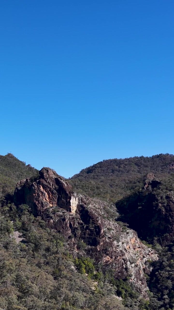 Inquadratura ampia statica di formazioni rocciose vulcaniche e foresta di eucalipti sotto un cielo azzurro e limpido