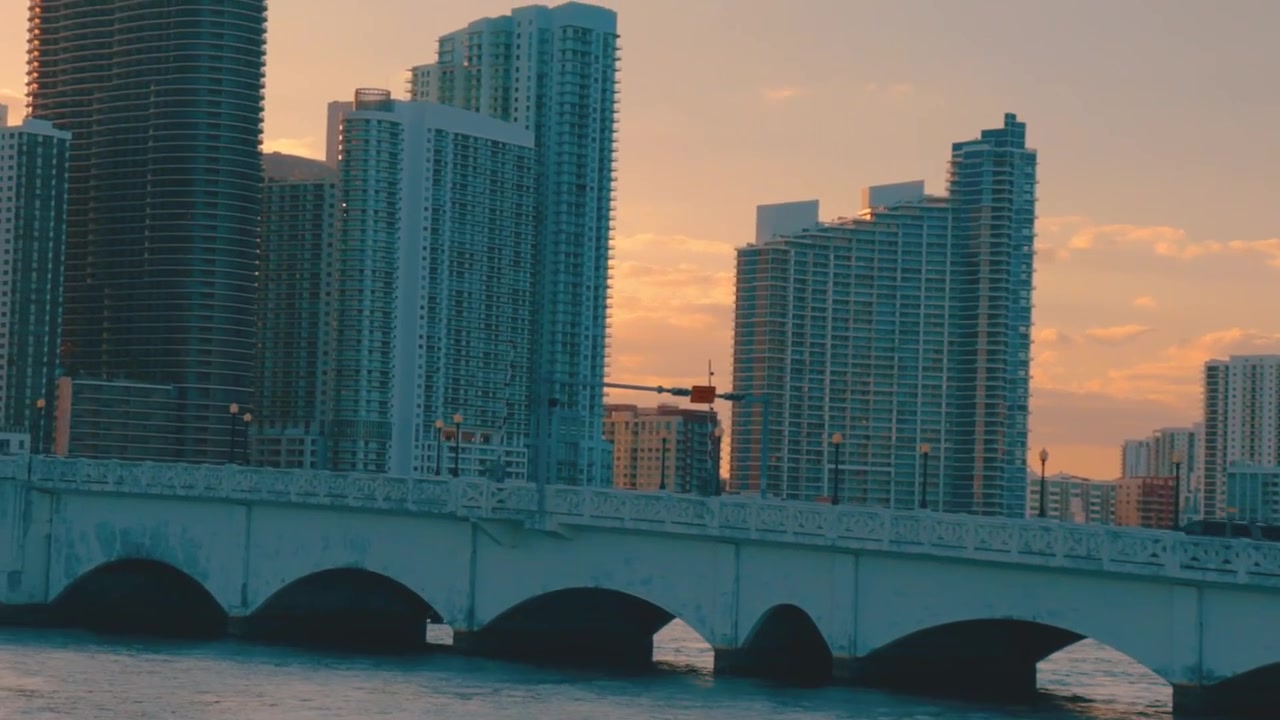 Carros atravessando a ponte leste da Venetian Causeway em Miami durante o pôr do sol, movendo-se para a esquerda e com panorâmica para cima