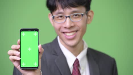 젊은 행복한 아시아 사업가 가 카메라 에 전화 를 보여주면서 미소 짓고 있다