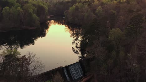 Lake-Placid-or-water-reservoir-with-a-dam-next-to-a-forest-at-sunset