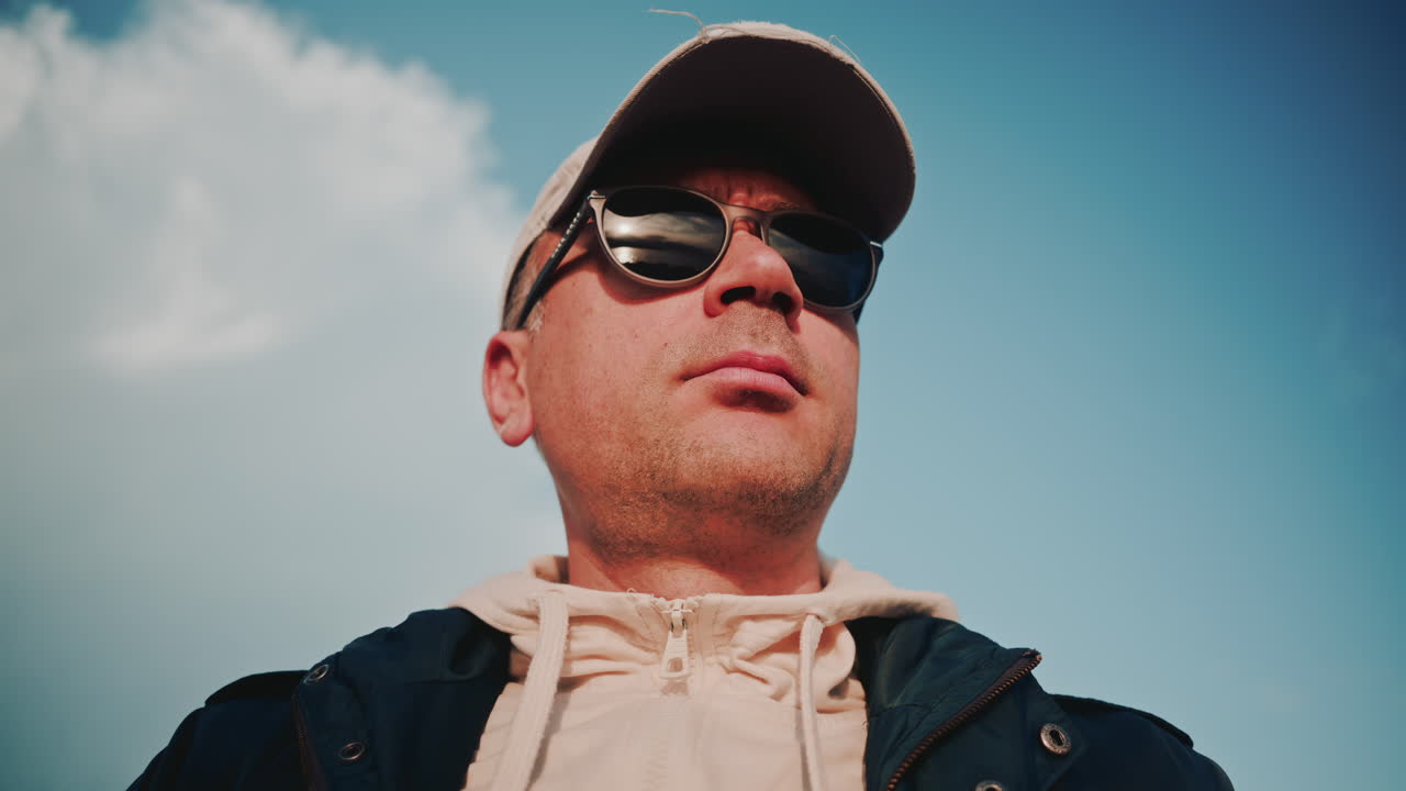 Close up portrait of a man wearing sunglasses and a cap, with the sky reflecting in the lenses