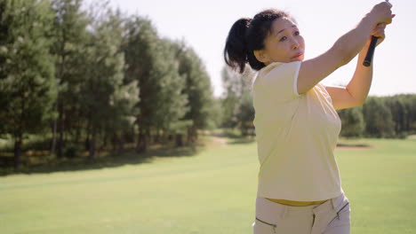 Mature-woman-practicing-golf-movements-on-grass-field
