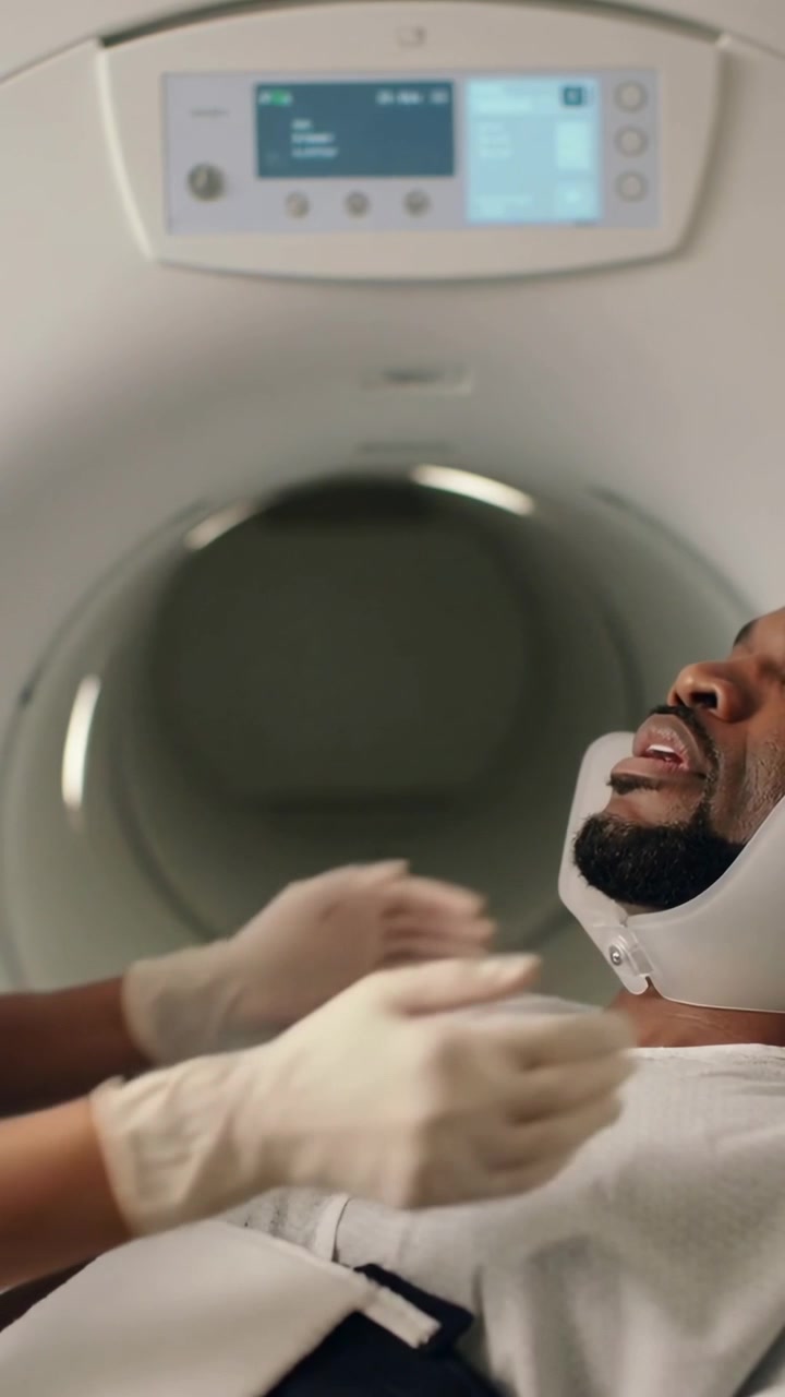 Video verticale: Preparazione di una TAC, tecnico guantato in camice che fissa il paziente nel supporto per la testa